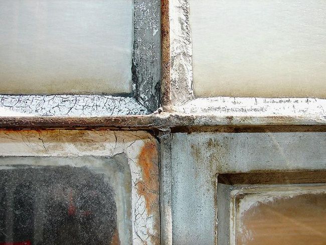 In einer Nahaufnahme ist ein altes Fensterkreuz zu sehen, dessen Gläser mit asbesthaltigem Material verkittet sind.