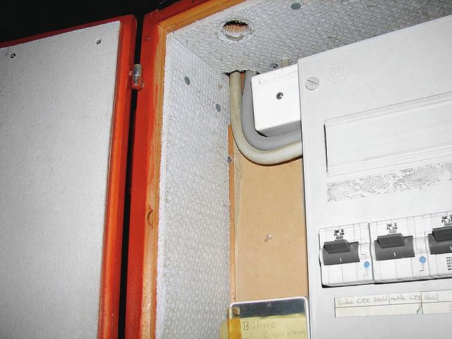 Blick in einen Sicherungskasten, der mit asbesthaltigen Platten isoliert wurde.