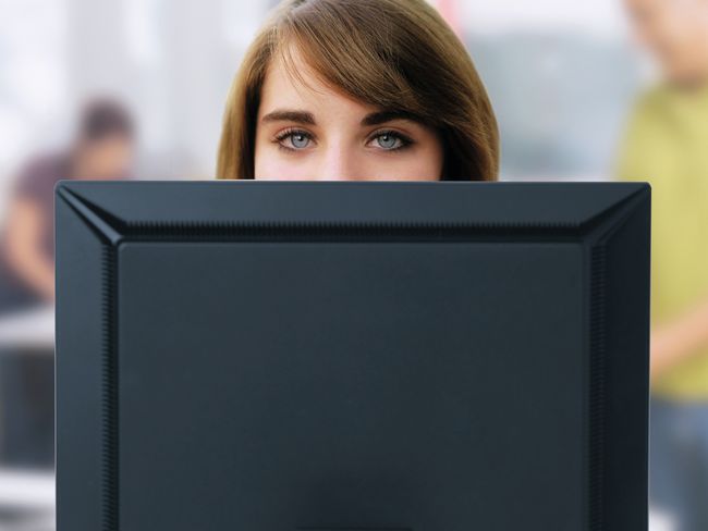 Eine junge Frau blickt über den Rand ihres Bildschirms. Die Oberkante liegt, ergonomisch korrekt, handbreit unter ihrer Augenhöhe.