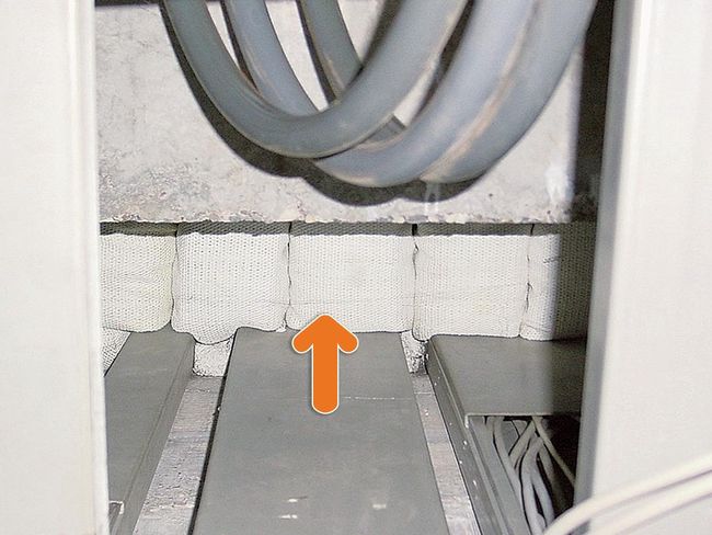 Ein orangefarbener Pfeil zeigt auf Asbestkissen, die zwischen einer Betonwand und dem Boden mit mehreren Kabelkanälen sitzen.